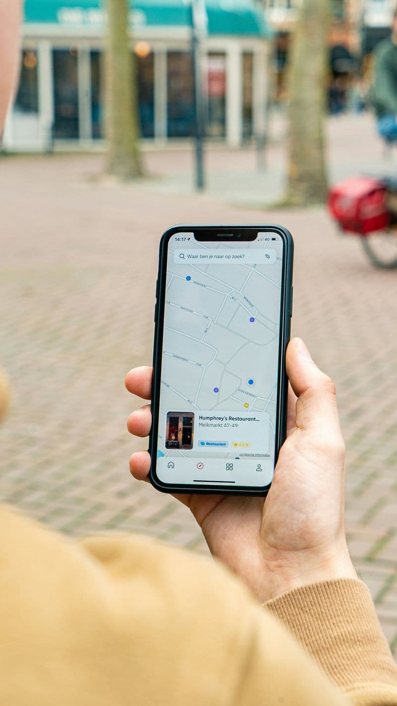 Pessoa na rua segurando o celular com um mapa de busca local aberto na tela